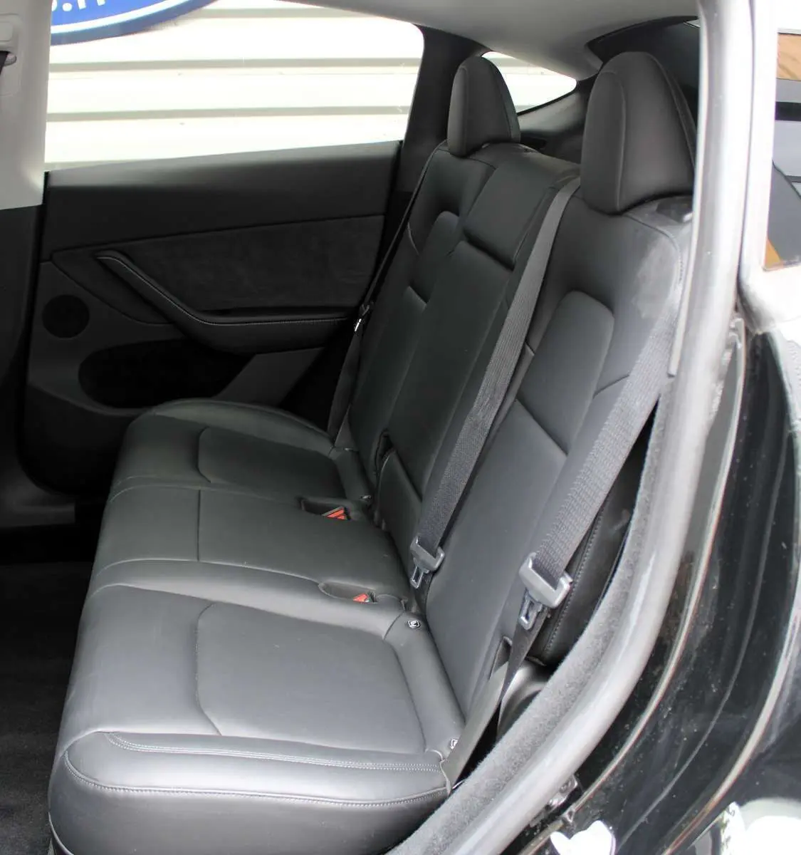 Vue latérale droite de l'intérieur arrière du Tesla Model Y 2024 noir métal avec sièges en cuir noir et ceintures de sécurité.