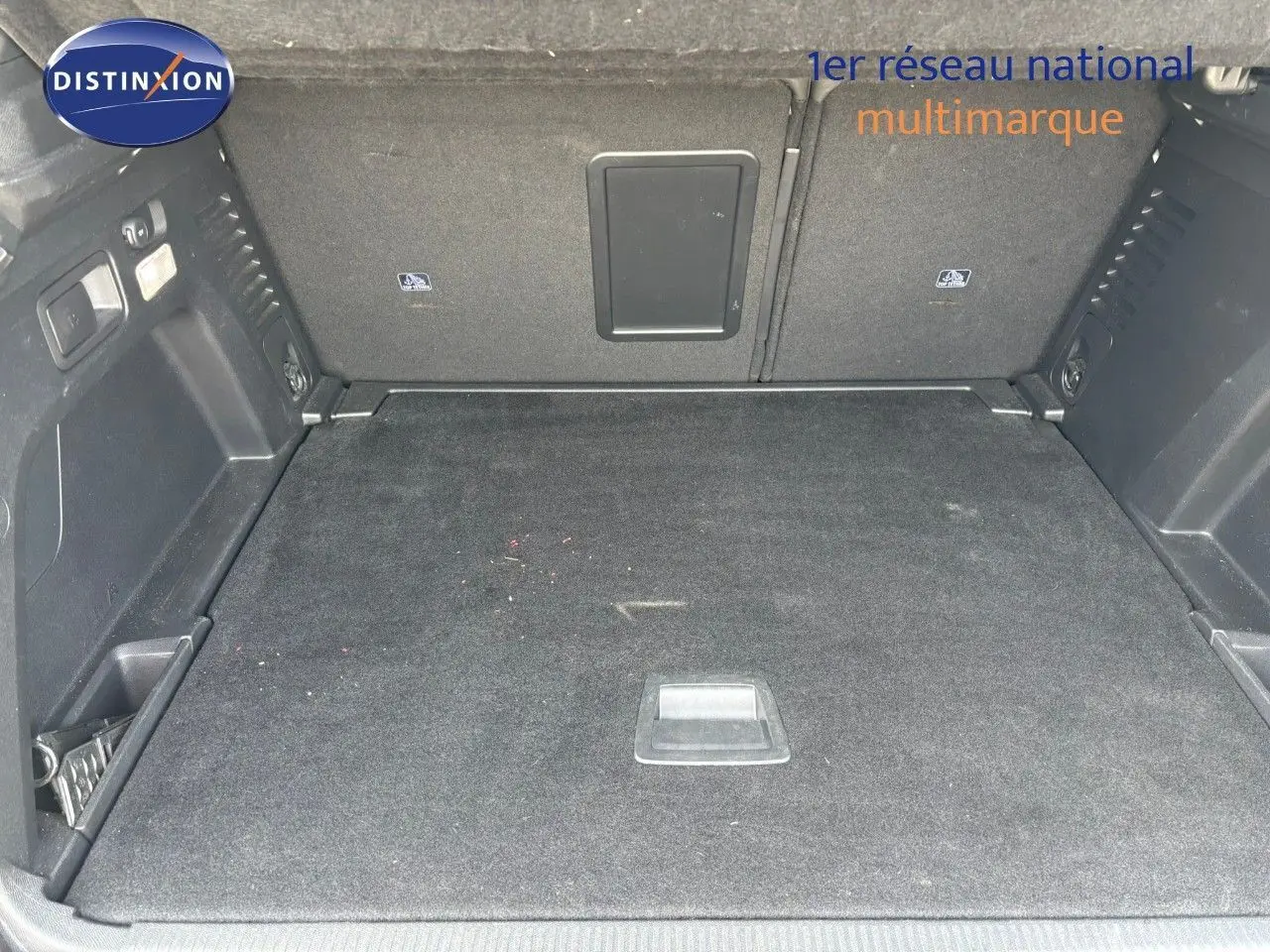 Coffre spacieux et propre du Peugeot 3008 GT blanc nacré, vue intérieure arrière avec tapis noir et rangements latéraux.