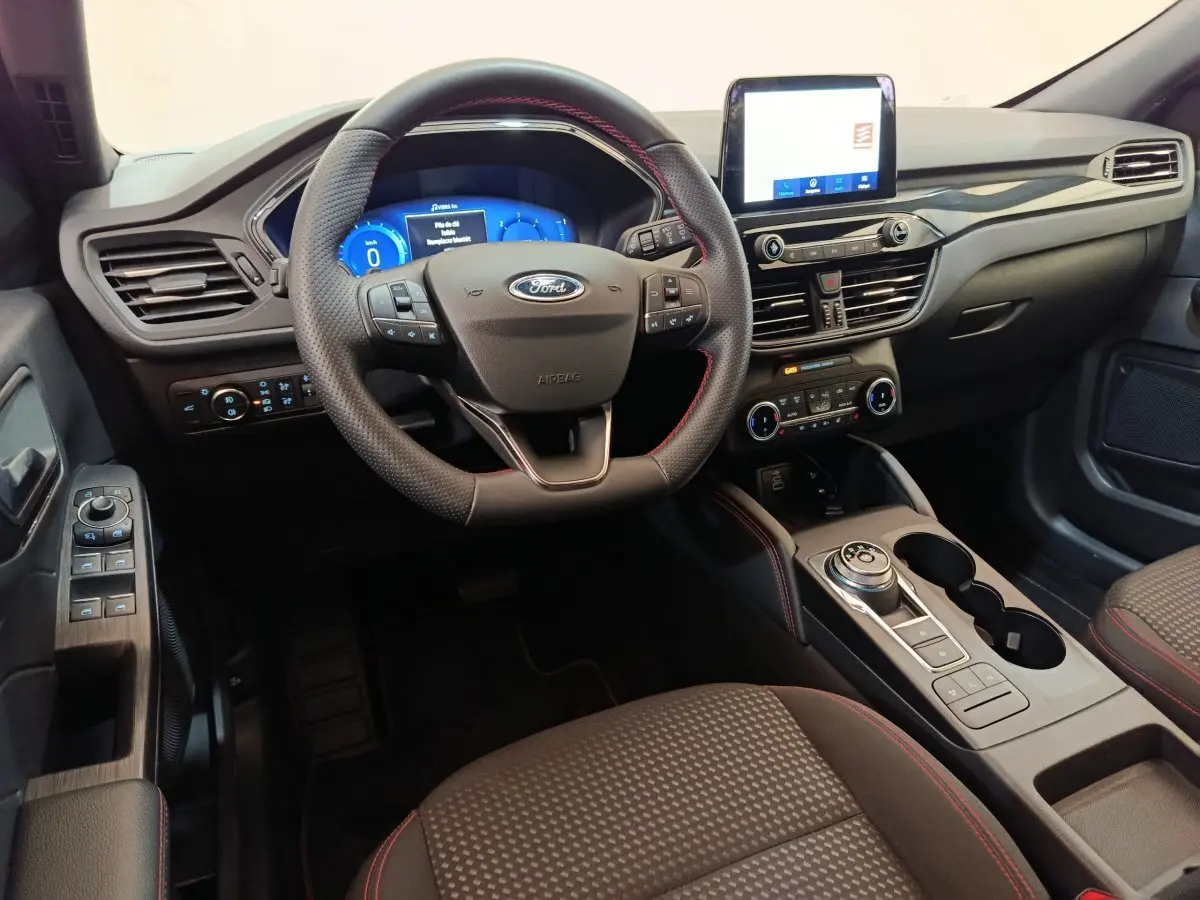 Intérieur du Ford Kuga 2024 vue côté conducteur, tableau de bord noir avec écran tactile et volant cuir noir.