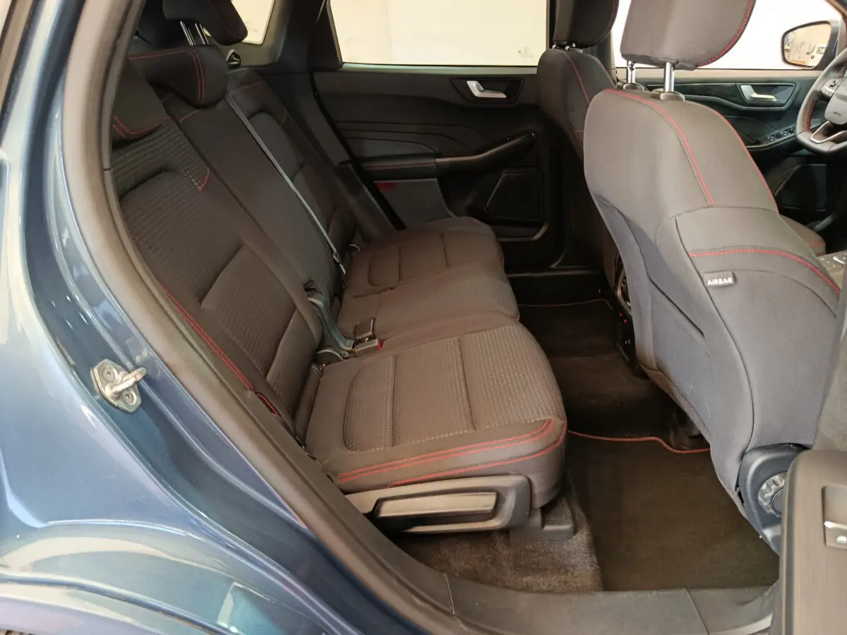 Vue intérieure côté gauche sur la banquette arrière noire avec surpiqûres rouges du Ford Kuga 2024 bleu St Line.