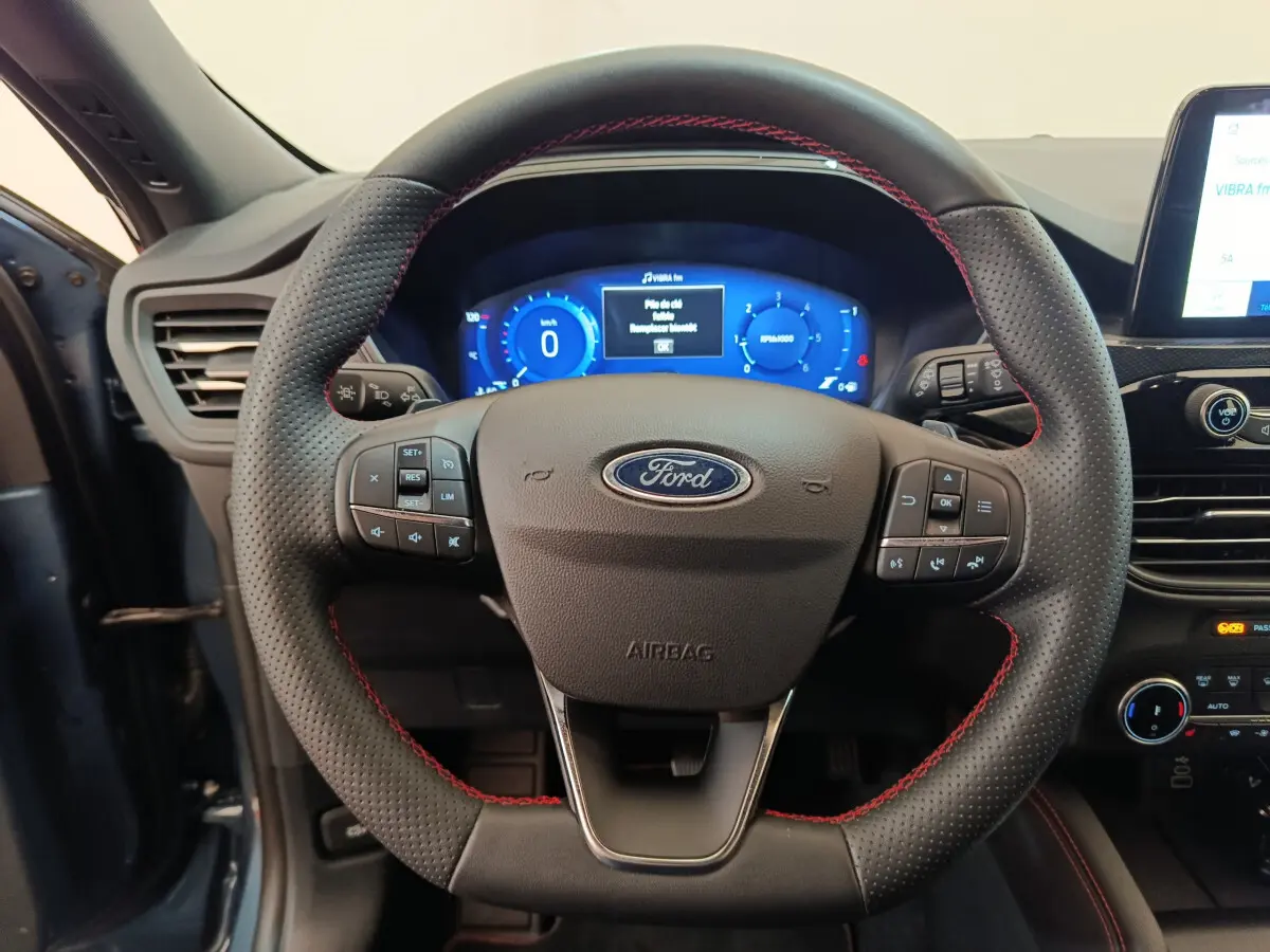 Volant en cuir noir avec surpiqûres rouges du Ford Kuga 2024, tableau de bord numérique bleu en arrière-plan.