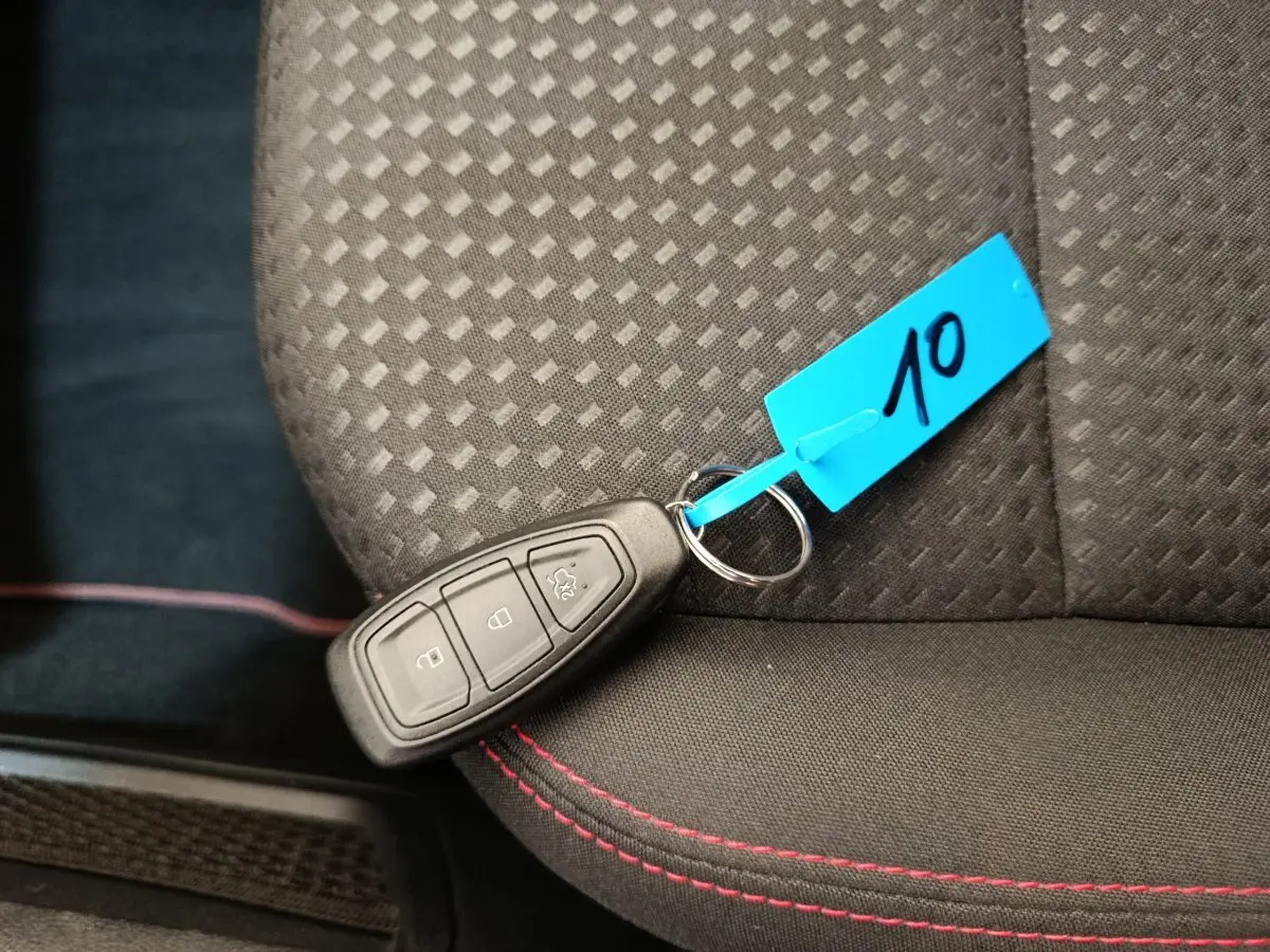 Clé de démarrage Ford Kuga 2024 posée sur siège tissu noir avec surpiqûres rouges, vue en plongée rapprochée.