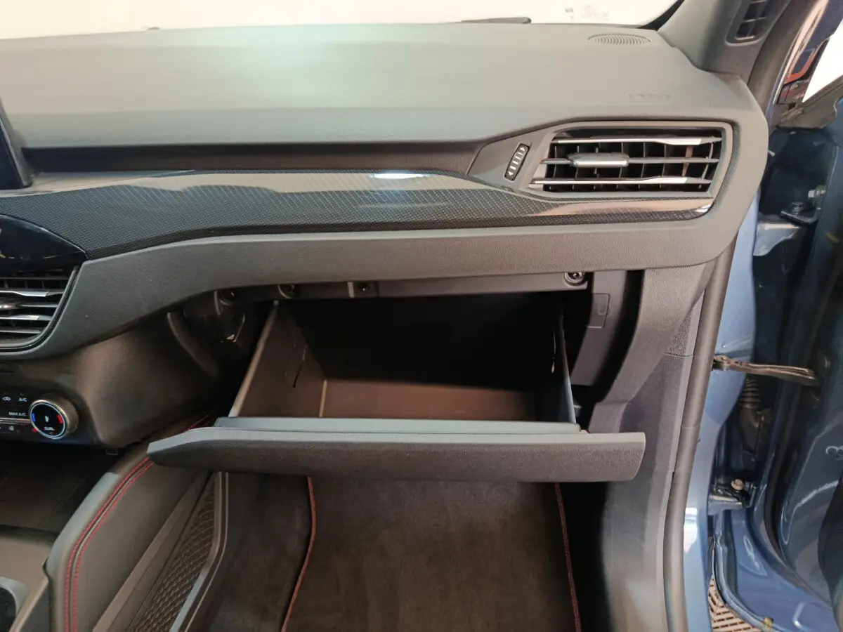 Intérieur côté passager du Ford Kuga bleu 2024, boîte à gants ouverte sous la planche de bord noire avec surpiqûres rouges.