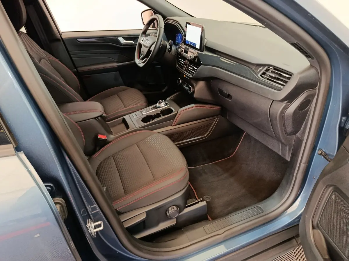 Intérieur avant droit du Ford Kuga bleu 2024 avec sièges noirs surpiqués rouges et écran tactile central.