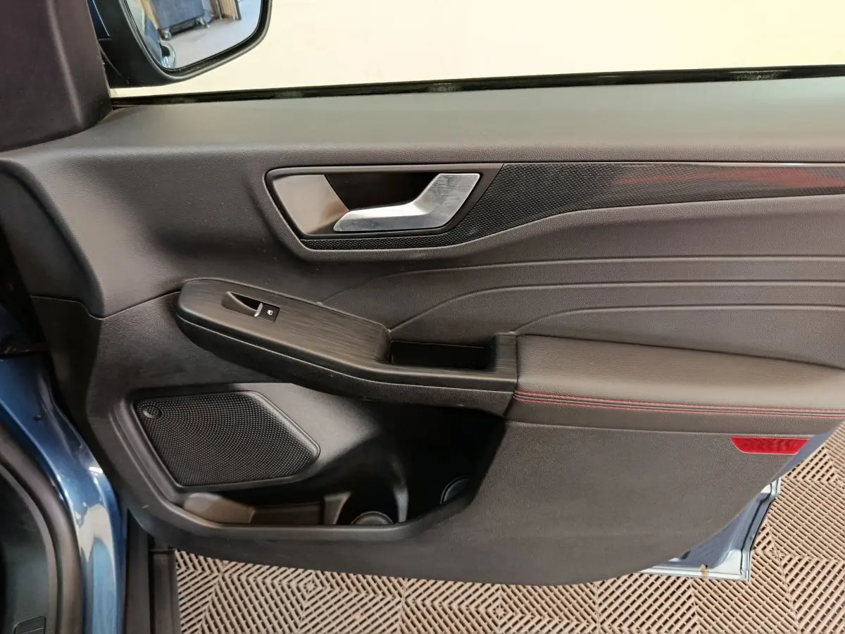 Intérieur côté gauche de la porte avant d'un Ford Kuga bleu 2024 avec garniture noire et surpiqûres rouges.