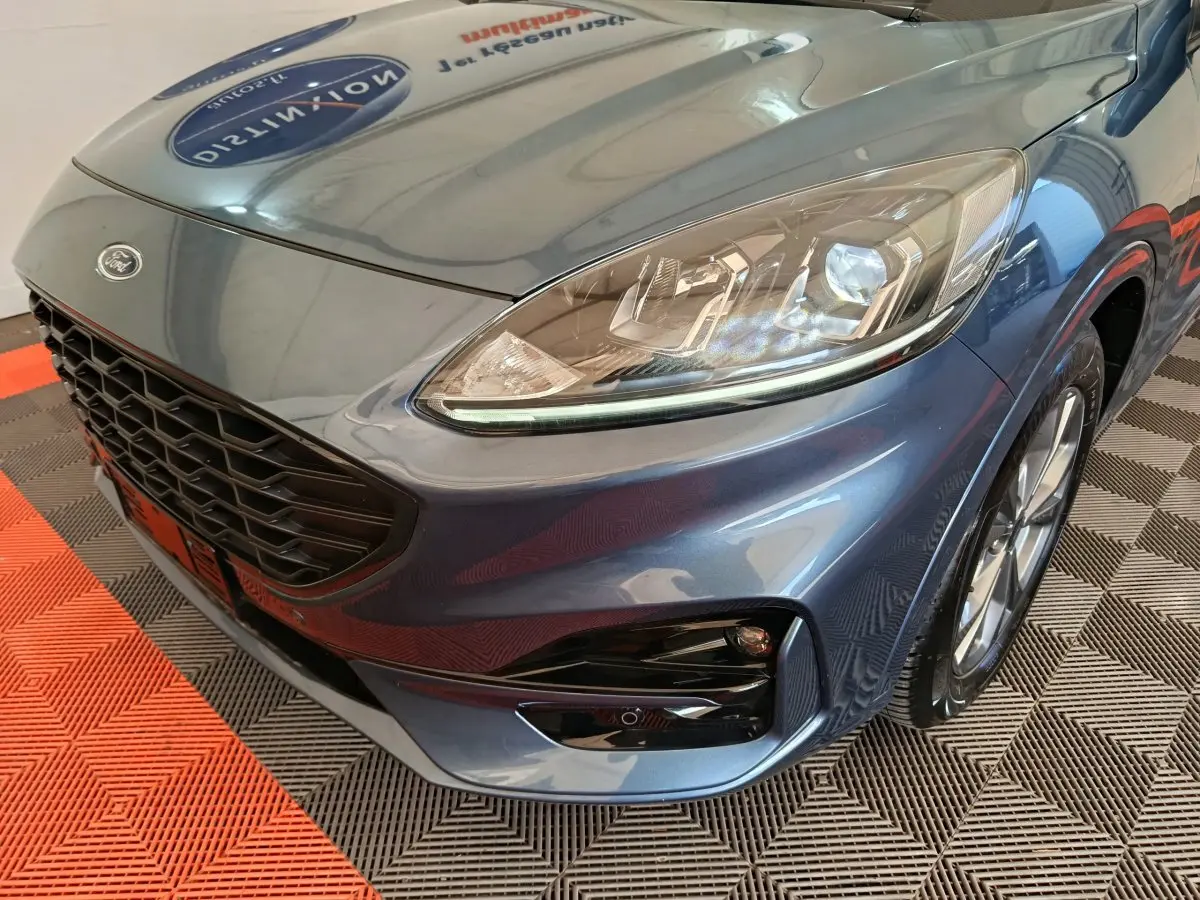 Vue en 3/4 avant droit d'un Ford Kuga bleu 2024 avec calandre noire et phares LED distinctifs.