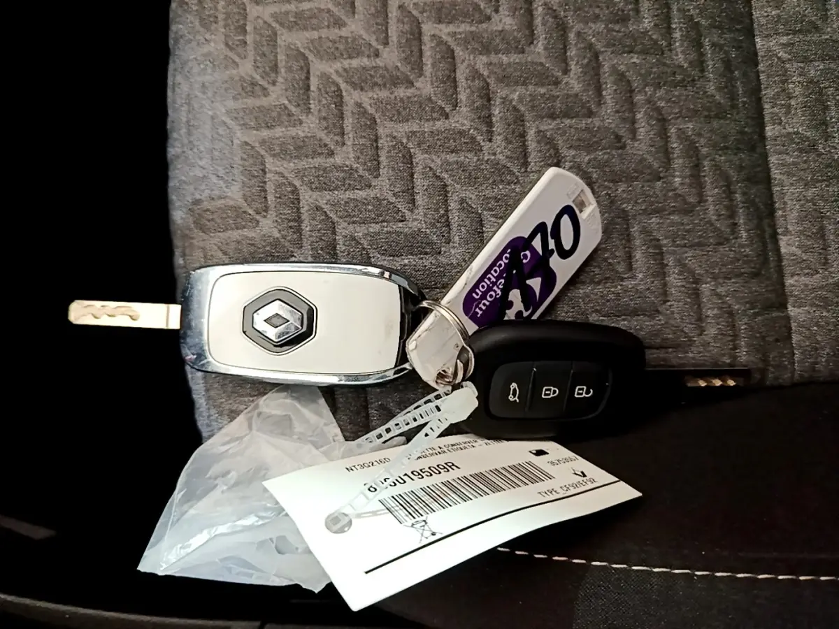 Clé Renault grise et noire posée sur un siège tissu gris à motif chevrons, avec porte-clés et étiquette.