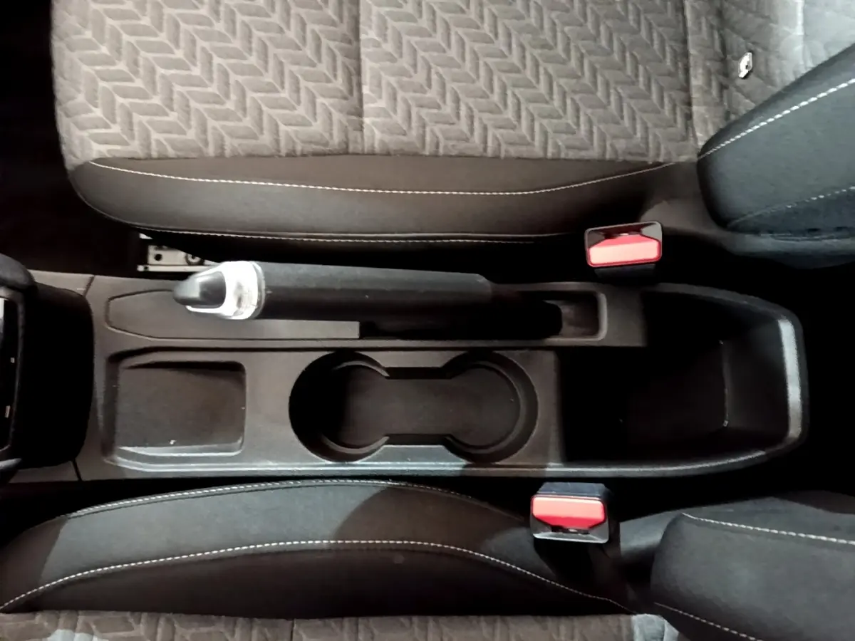 Vue plongeante sur la console centrale noire de la Renault Clio gris foncé avec frein à main manuel et porte-gobelets.