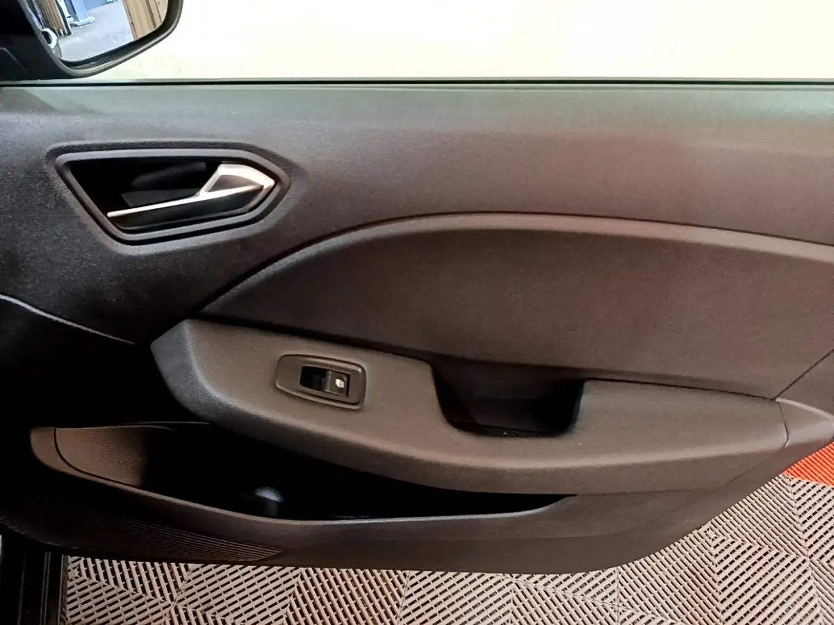 Vue intérieure du panneau de porte côté conducteur de la Renault Clio gris foncé avec poignée argentée et commande de fenêtre électrique.