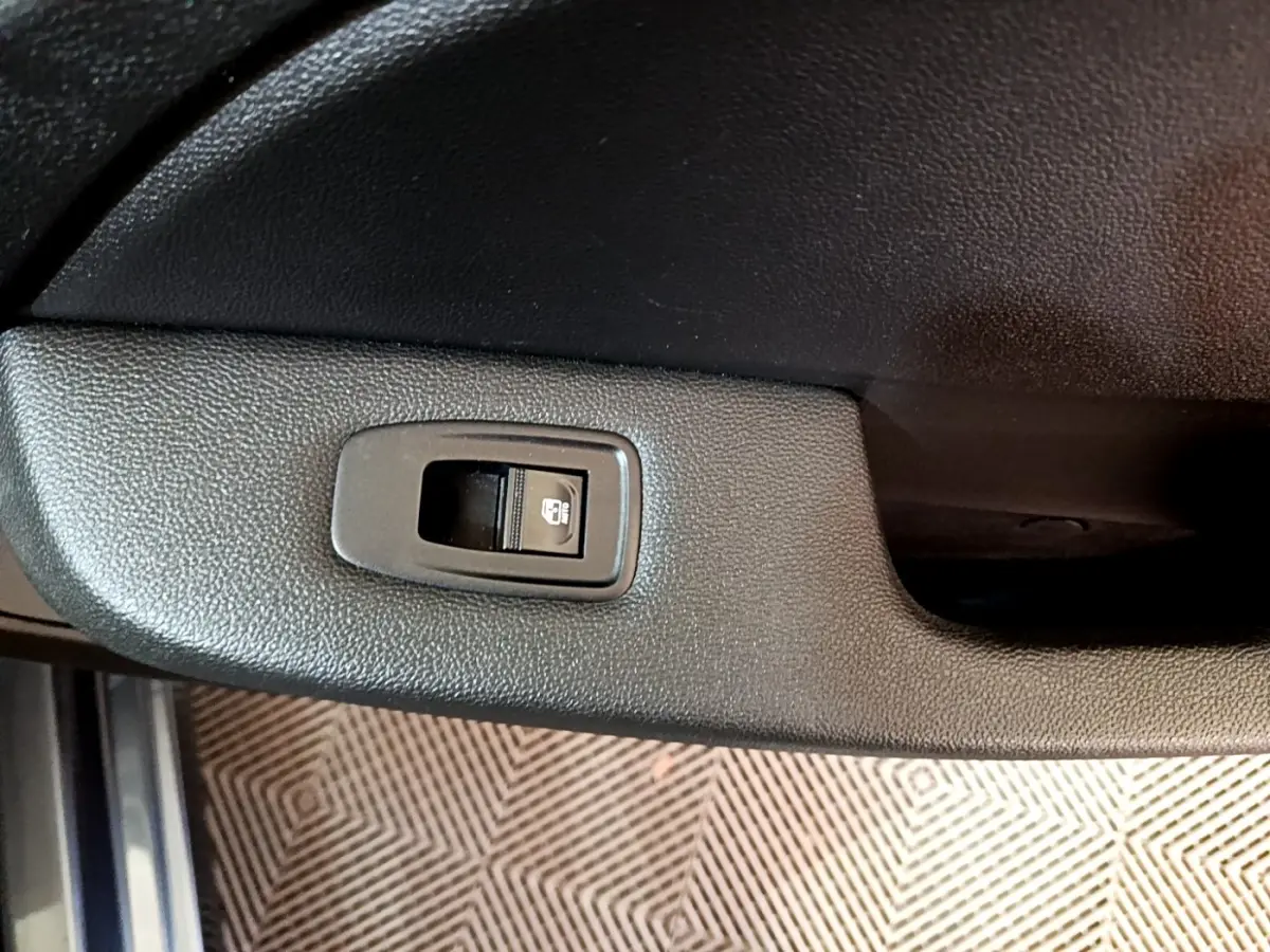 Gros plan sur le bouton de verrouillage centralisé dans la portière intérieure noire d’une Renault Clio gris foncé.