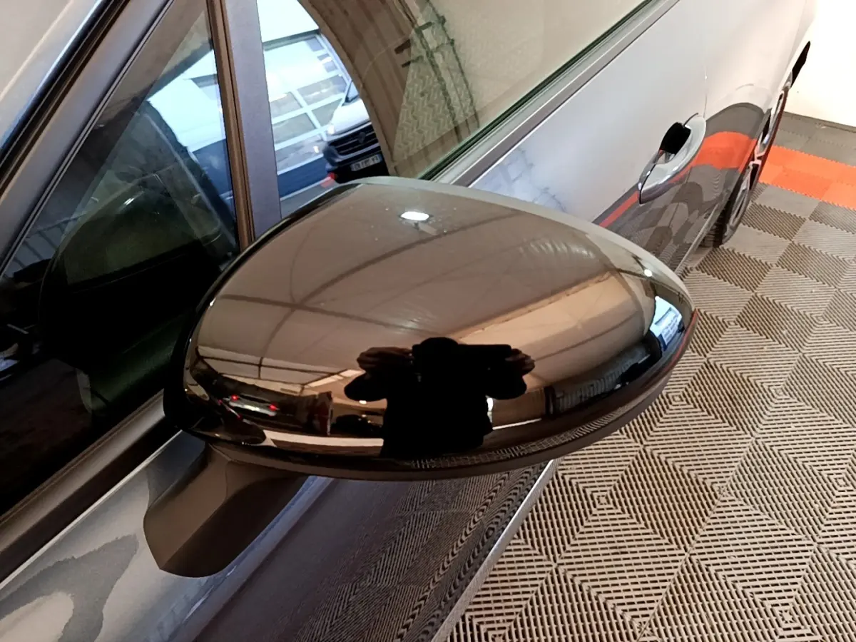 Gros plan sur le rétroviseur droit noir brillant d'une Renault Clio gris foncé, vue latérale en intérieur.