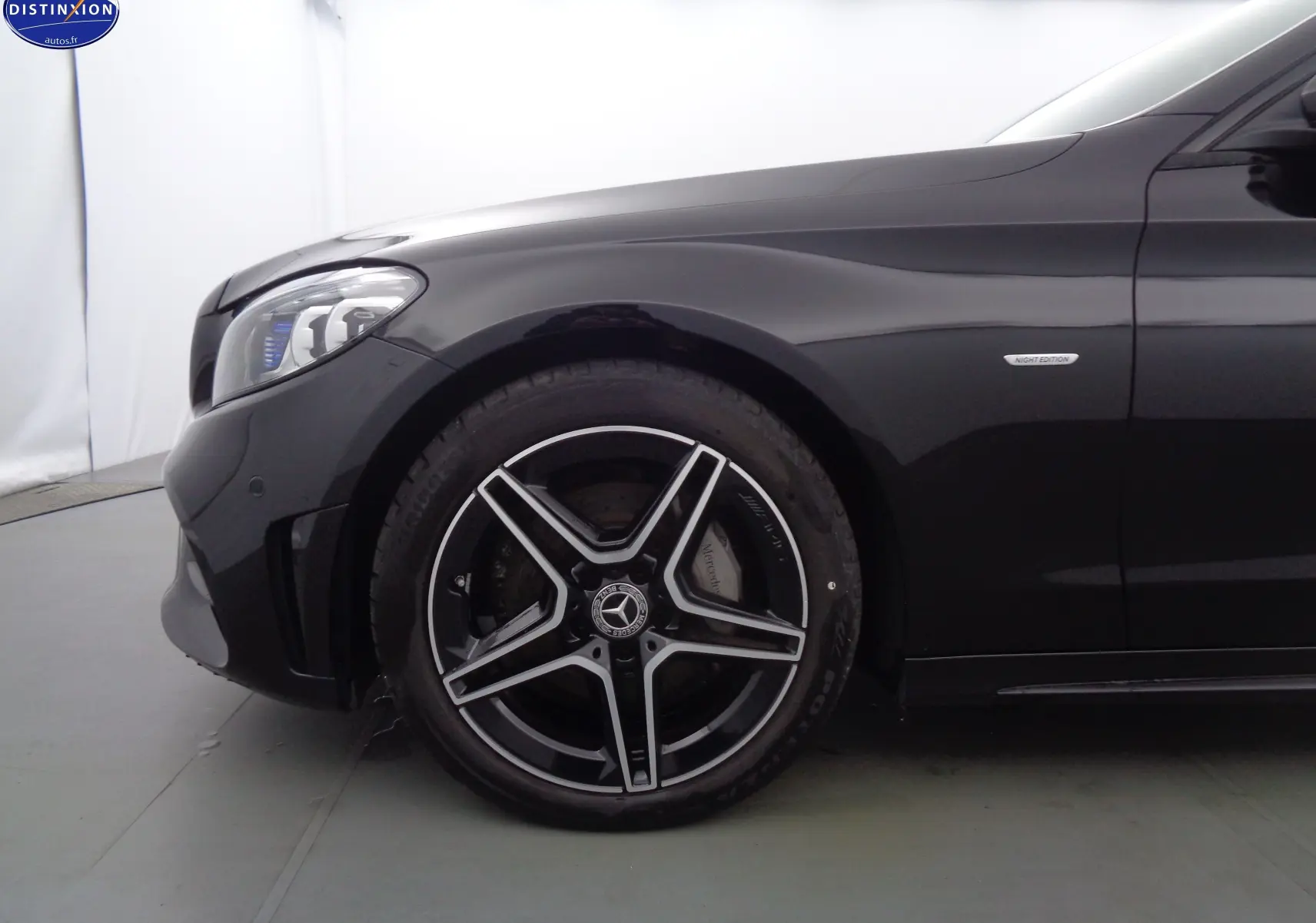 Gros plan sur la roue avant gauche et l'aile noire métallisée d'une Mercedes Classe C Break 220D AMG Line avec badge Night Edition.