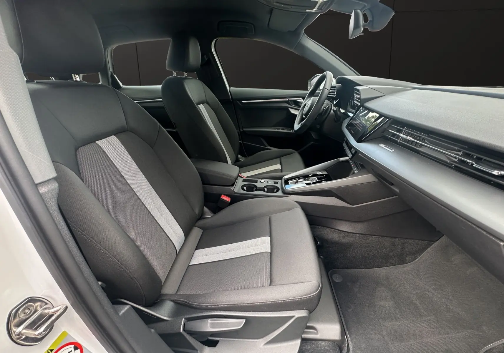 Intérieur avant côté conducteur de l'Audi A3 Sportback 2024 en tissu noir avec bande grise centrale et tableau de bord moderne.