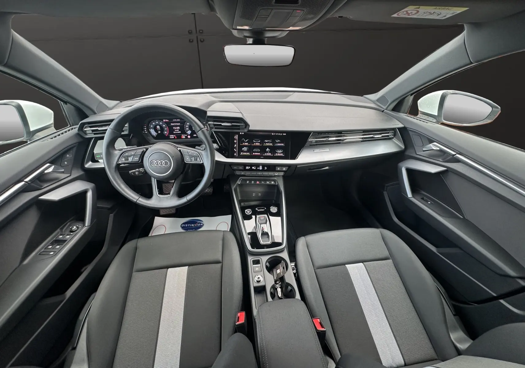 Intérieur noir de l'Audi A3 Sportback 2024 vu de face, avec tableau de bord digital et sièges tissu à bande grise centrale.