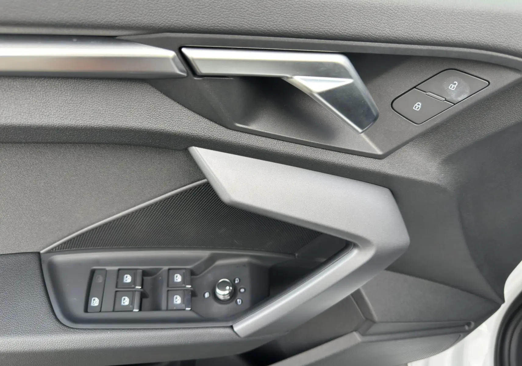 Détail de la porte côté gauche de l'Audi A3 Sportback blanc Arkona 2024 avec commandes électriques et poignée argentée.