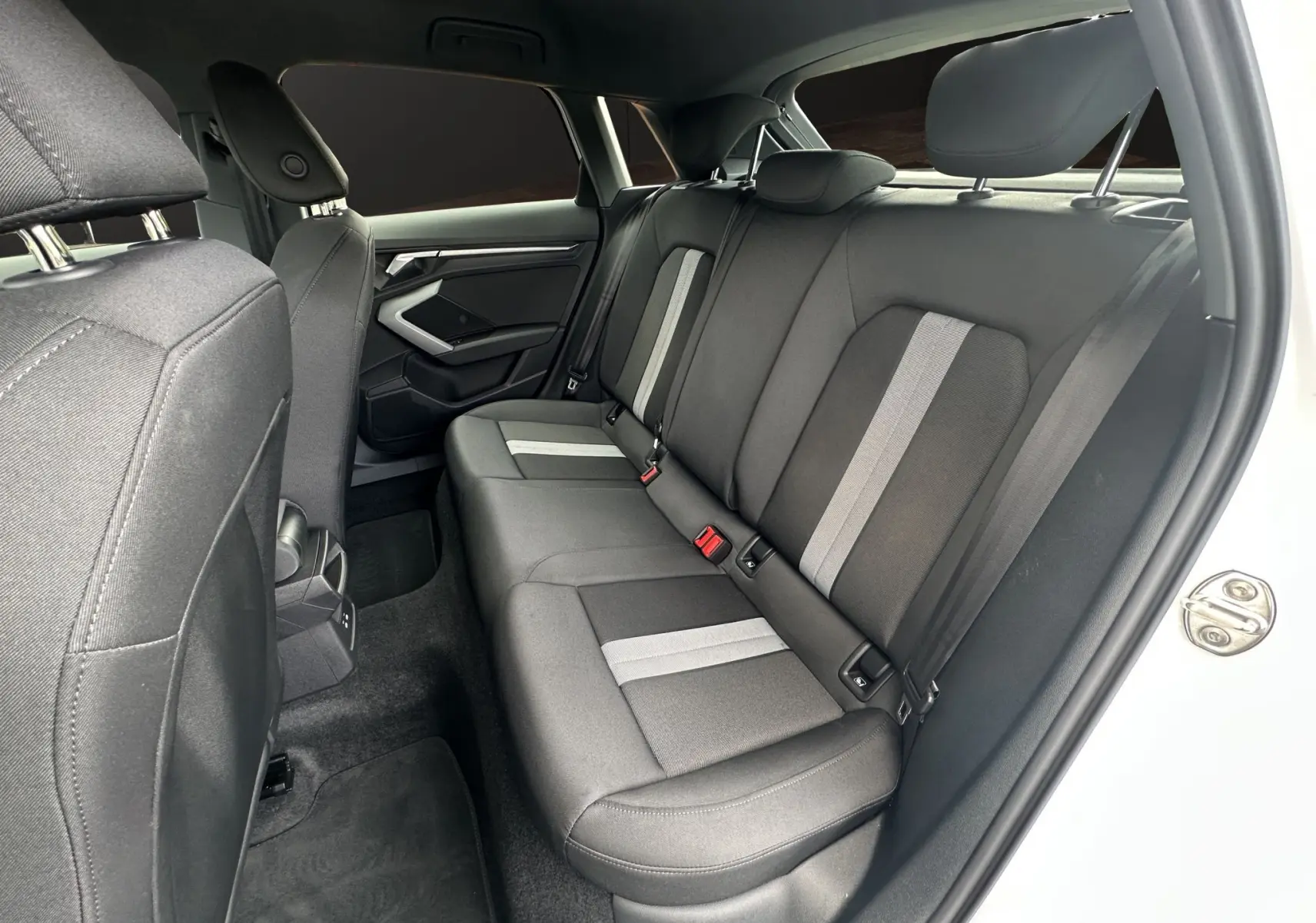Vue côté gauche de l'intérieur arrière de l'Audi A3 Sportback 2024 blanc Arkona avec sièges tissu noir à bandes grises.