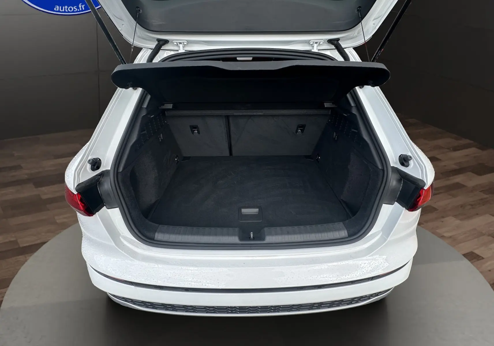 Coffre ouvert vu de l'arrière d'une Audi A3 Sportback 2024 blanc Arkona avec intérieur de coffre noir.