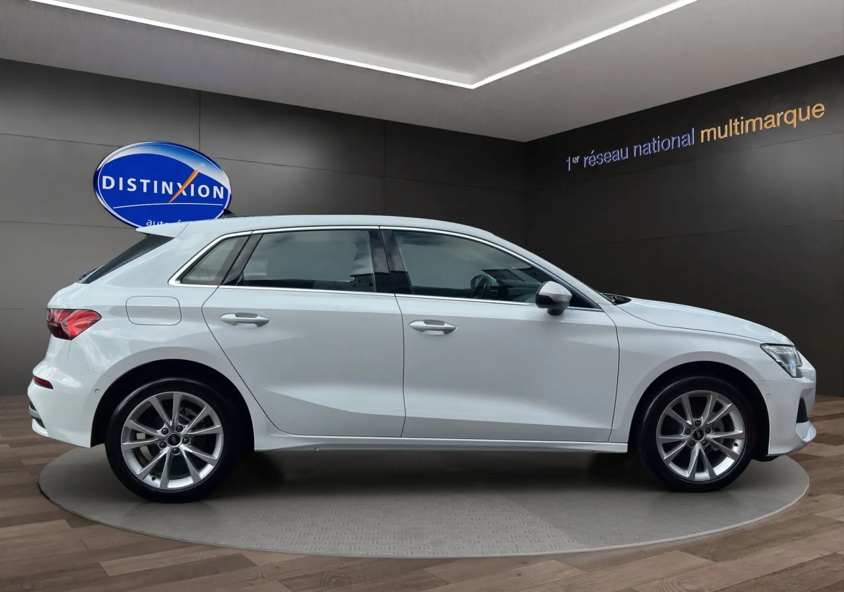 Profil côté gauche d'une Audi A3 Sportback blanche Arkona 2024 avec jantes alliage léger en showroom.