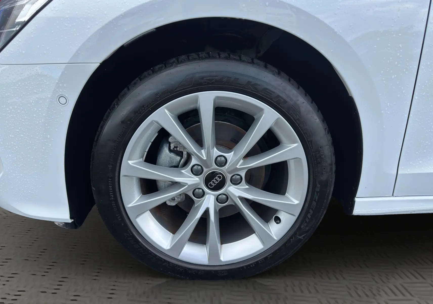 Gros plan sur la roue avant droite d'une Audi A3 Sportback blanche Arkona avec jante alliage léger à 10 branches.