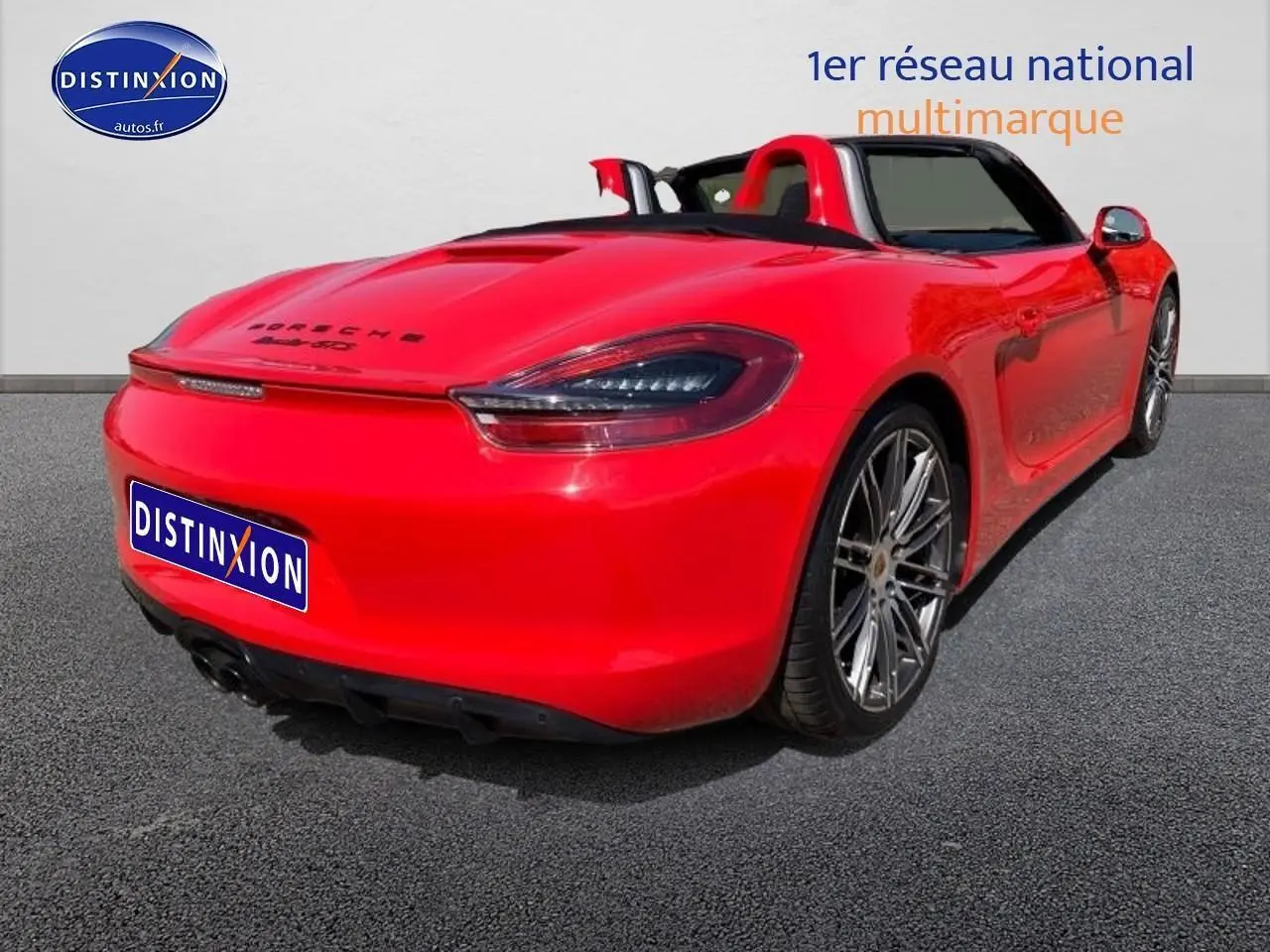 Vue 3/4 arrière droite d'une Porsche Boxster rouge cabriolet avec jantes alu et becquet arrière.
