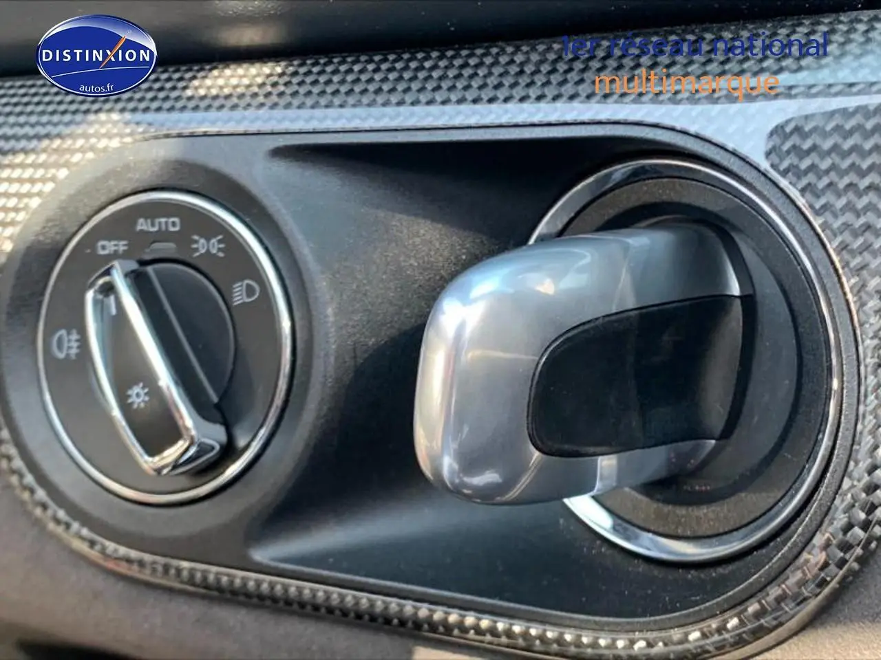 Gros plan sur la commande des phares et l'aération avec finition carbone dans l'habitacle noir de la Porsche Boxster rouge.