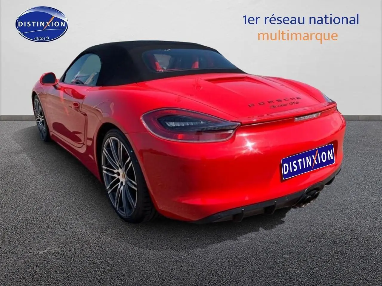 Vue 3/4 arrière droite d'une Porsche Boxster GTS rouge avec capote noire et jantes alu multibranches.
