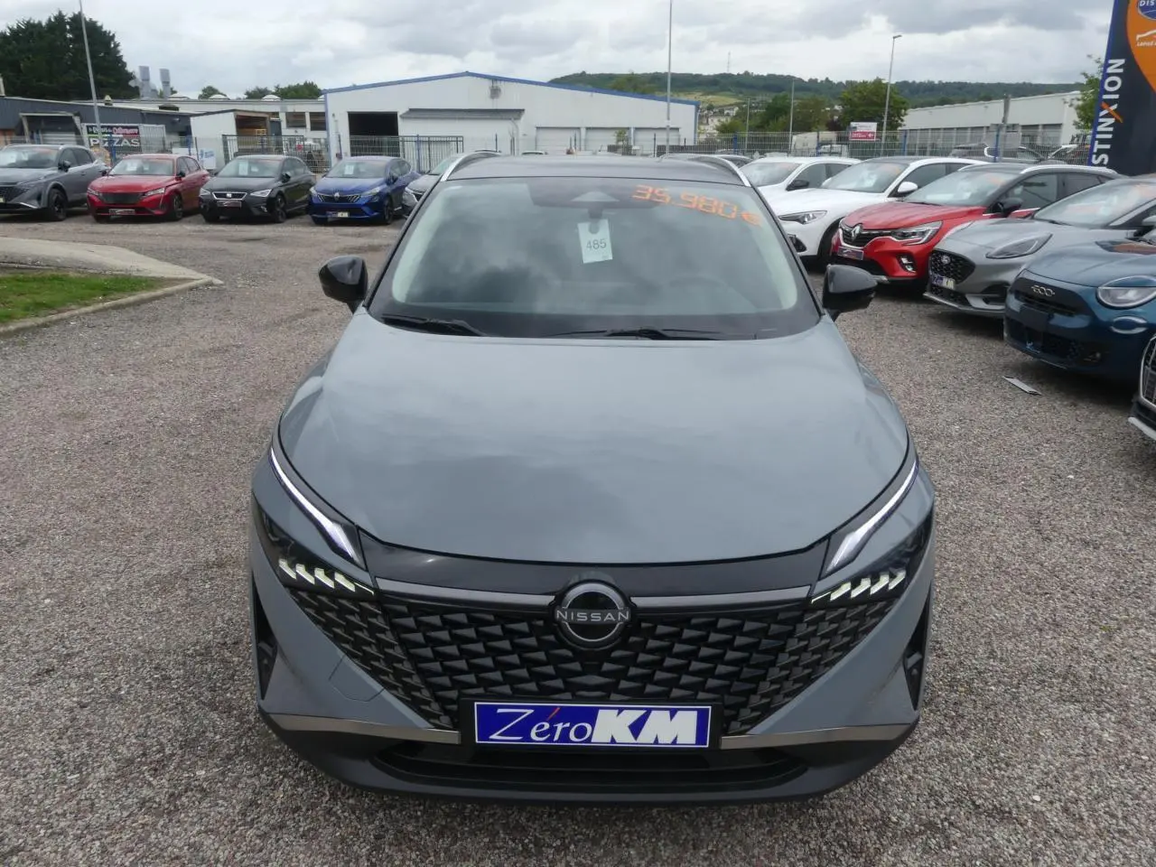 Vue avant d'un Nissan Qashqai gris métallisé avec calandre noire et feux LED distinctifs sur un parking.