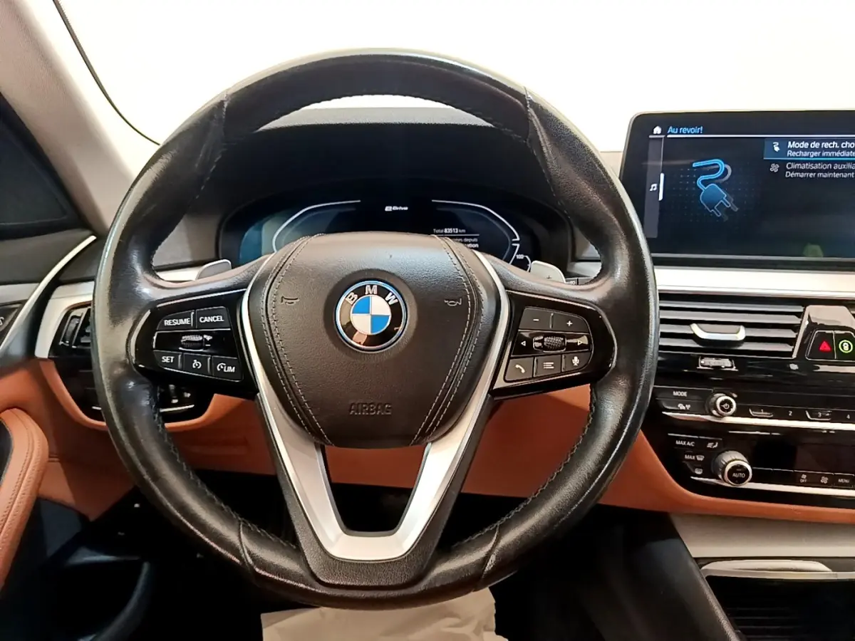 Vue intérieure centrée sur le volant cuir noir et le tableau de bord marron de la BMW Série 5 Touring 530e hybride rechargeable.