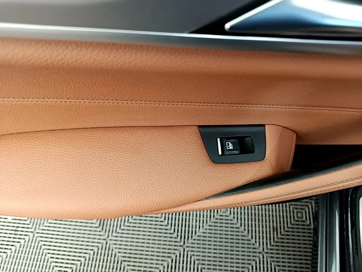 Gros plan sur la commande de lève-vitre intégrée dans la garniture cuir marron clair de la porte avant droite d'une BMW Série 5 Touring.