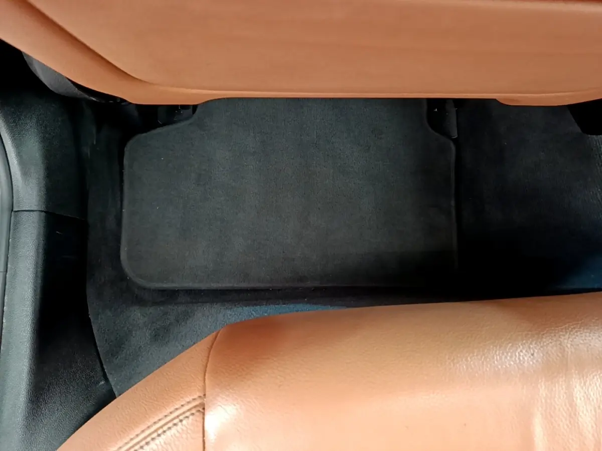 Détail du sol arrière avec tapis noir et sellerie cuir marron clair dans une BMW Série 5 Touring 530e hybride 2022.
