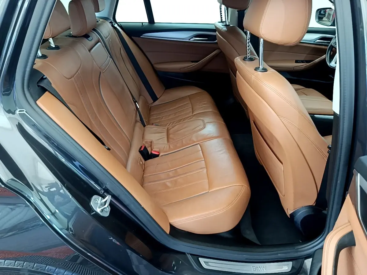 Vue intérieure côté gauche montrant les sièges arrière en cuir marron clair d'une BMW Série 5 Touring gris clair.