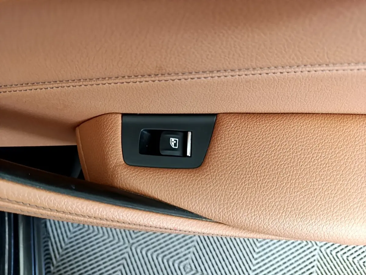 Détail de la commande d'ouverture électrique du coffre sur la garniture cuir marron clair d'une BMW Série 5 Touring 530e 2022.