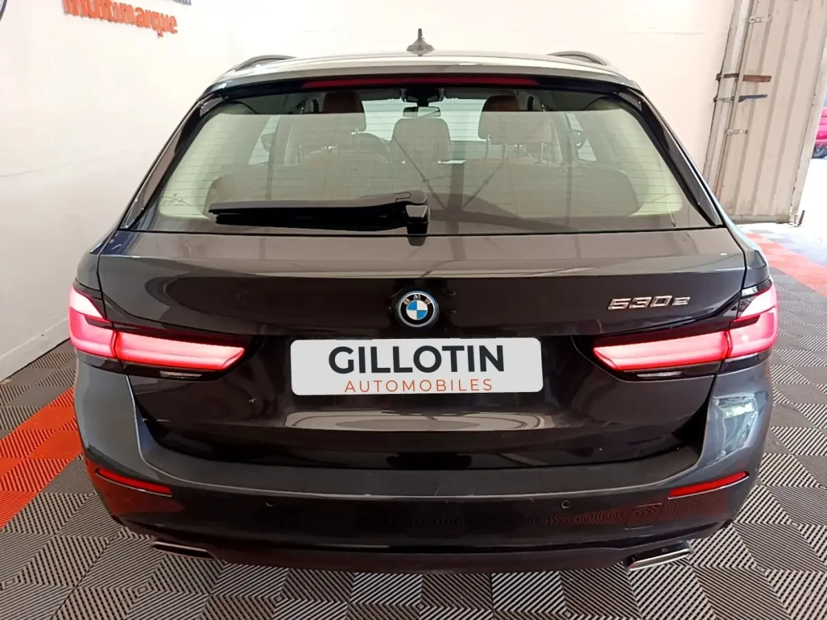 Vue arrière d’une BMW Série 5 Touring 530e gris clair avec feux LED allumés et logo visible sur coffre.