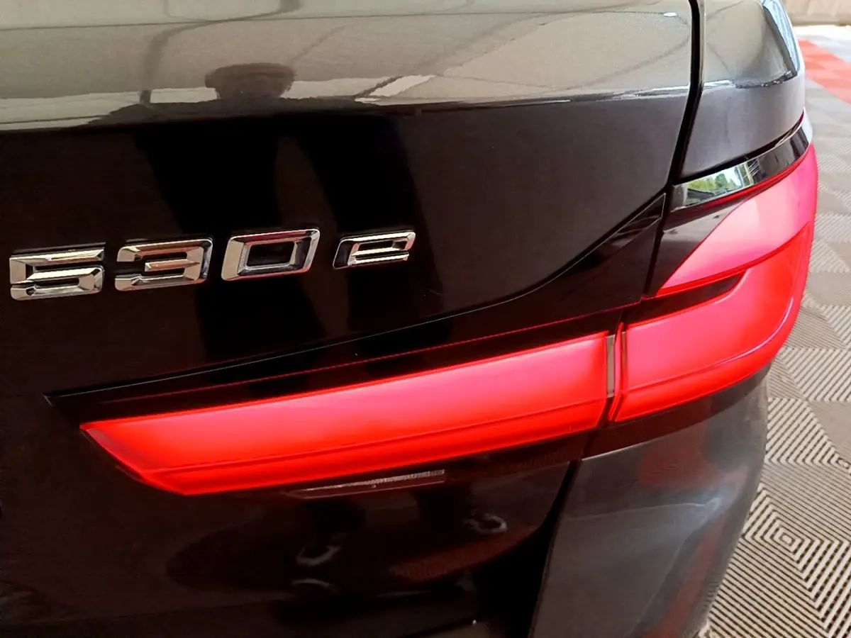 Gros plan sur le feu arrière droit rouge et le badge 530e d'une BMW Série 5 Touring gris foncé.