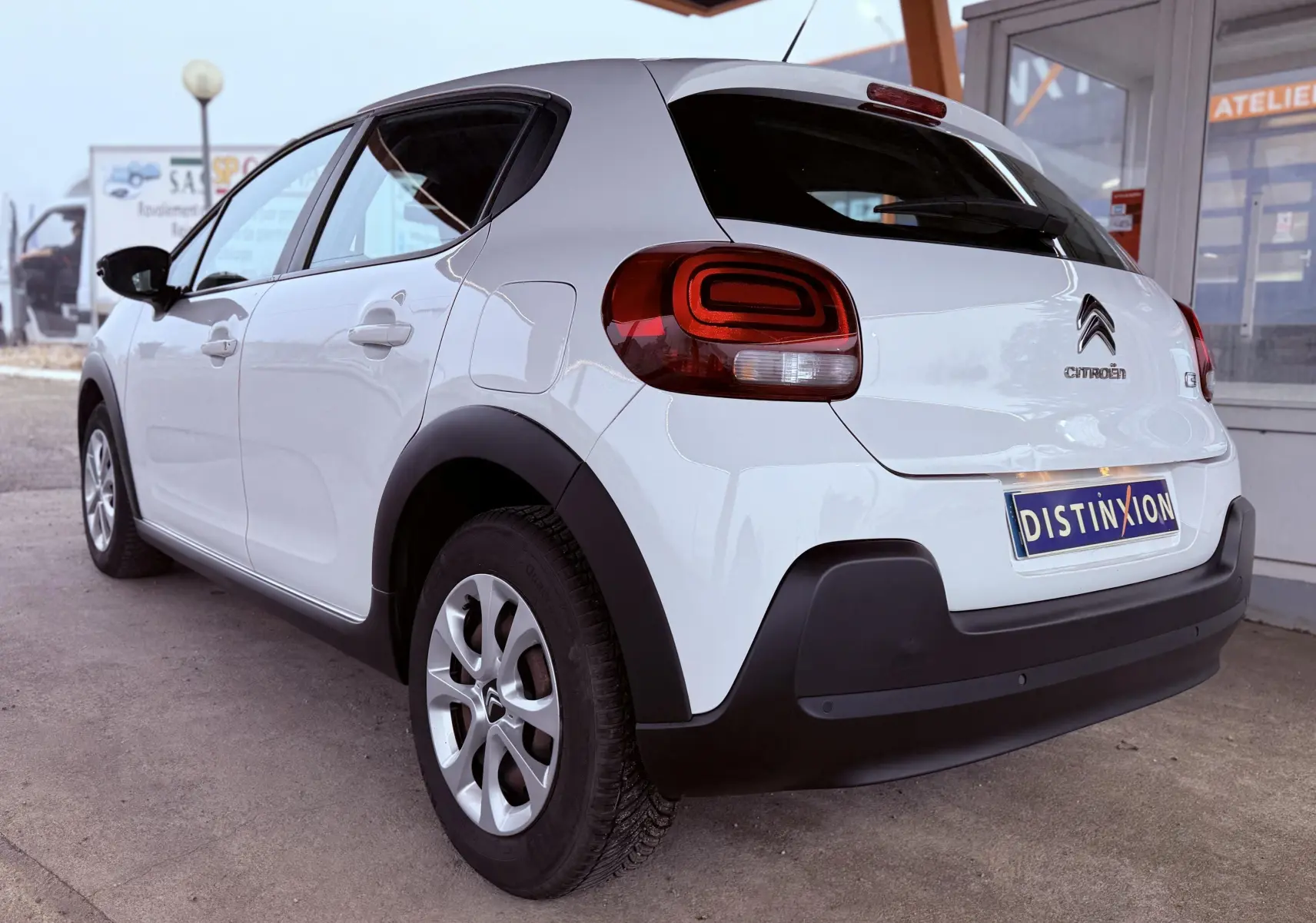 Vue 3/4 arrière droite d'une Citroën C3 Société blanche de 2019 avec feux arrière distinctifs et protections noires.