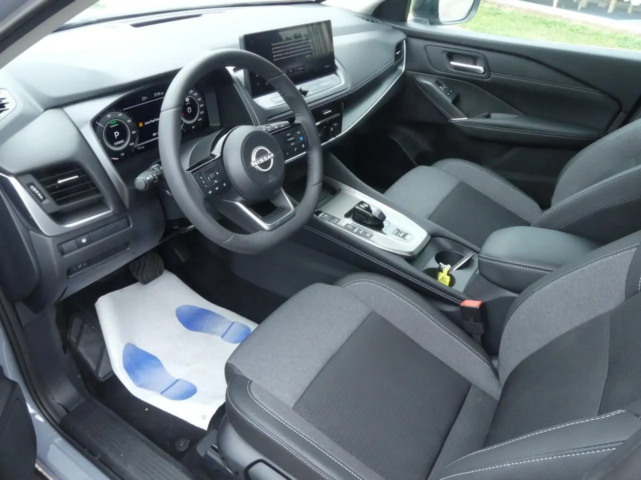 Intérieur avant du Nissan Qashqai 2025 gris, vue côté conducteur sur tableau de bord et sièges tissu noir et gris.
