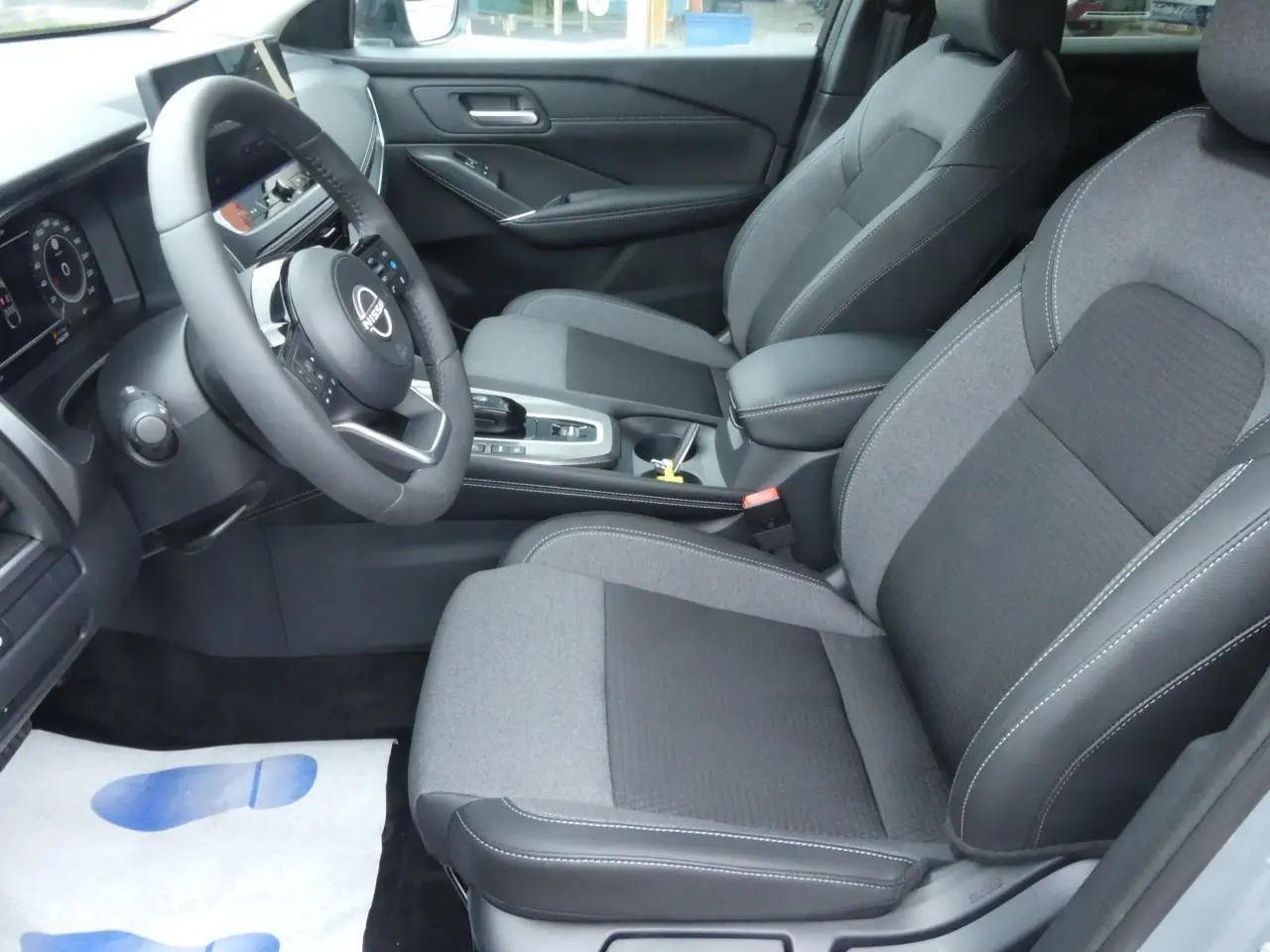 Intérieur avant du Nissan Qashqai 2025, sièges gris tissu et TEP, volant cuir, console centrale avec boîte auto.