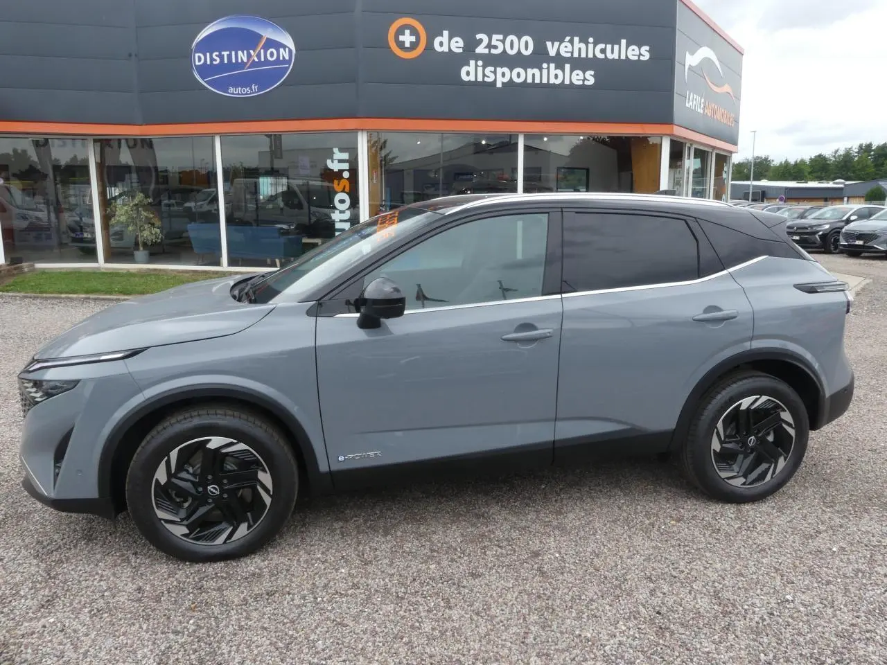 Nissan Qashqai 2025 gris métallisé, vue profil côté gauche, toit noir bi-ton et jantes alliage noires.