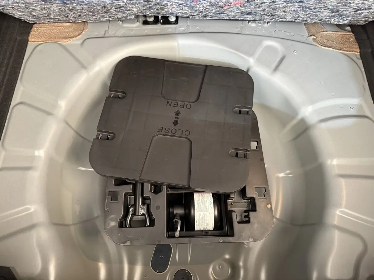 Compartiment de rangement sous le plancher du coffre de la Renault Clio noire, montrant le kit de réparation pneus.