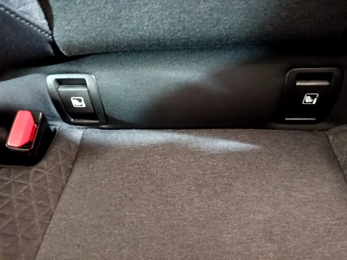 Détail de la banquette arrière noire de la Renault Clio Business TCe 100 avec boutons de rabattement et boucle de ceinture rouge.