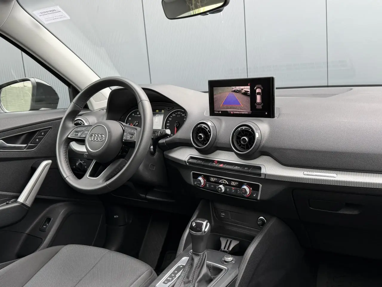 Intérieur Audi Q2 35 TFSI S-Line 2023, vue du poste de conduite avec écran caméra de recul et tableau de bord noir.
