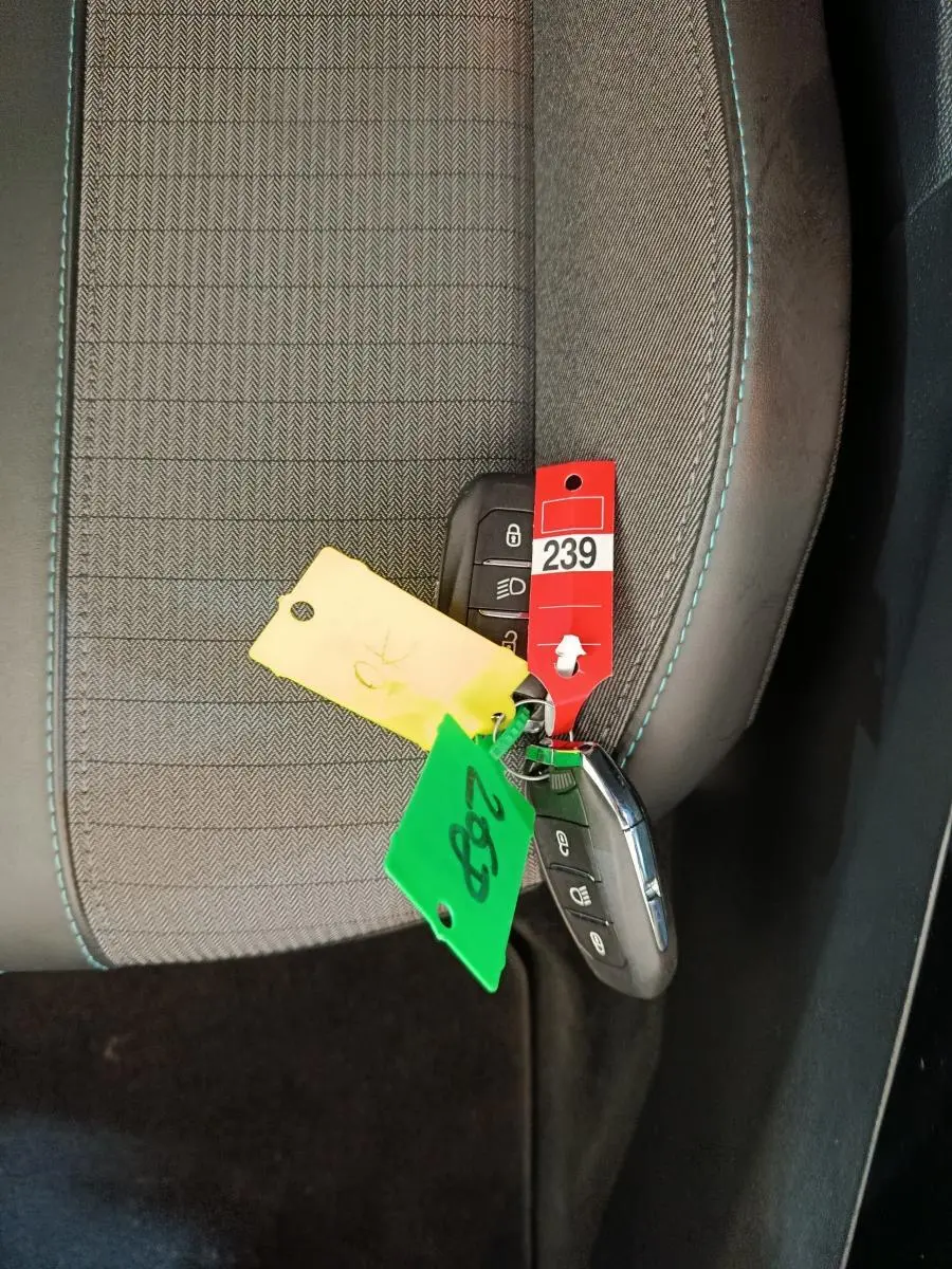 Gros plan sur la clé de Peugeot 208 posée sur un siège tissu gris avec surpiqûres bleues, intérieur sombre.