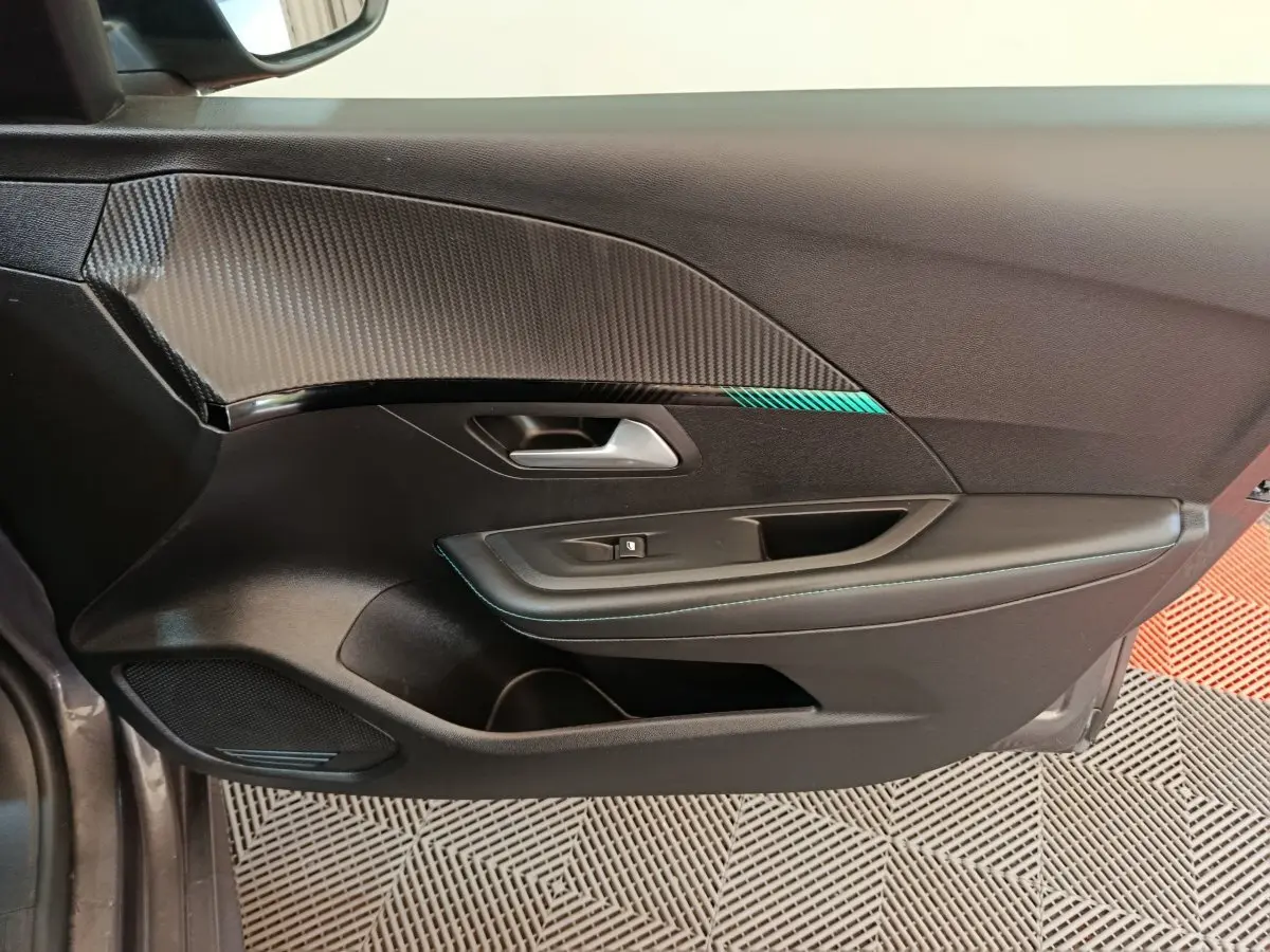 Vue rapprochée de la porte intérieure côté conducteur de la Peugeot 208 2020 avec insert carbone et surpiqûres bleues.