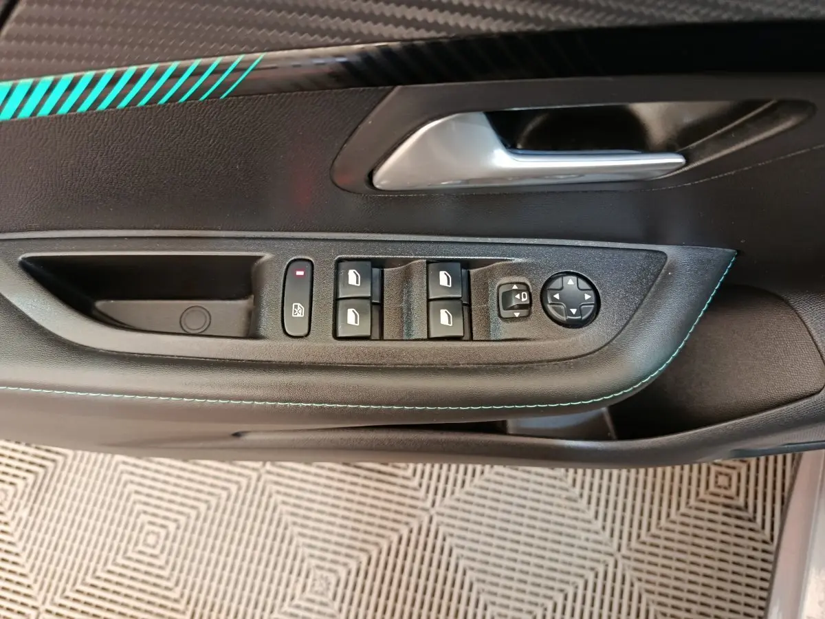 Vue rapprochée de la porte côté conducteur d’une Peugeot 208 avec commandes de vitres et rétroviseurs, surpiqûres bleues visibles.