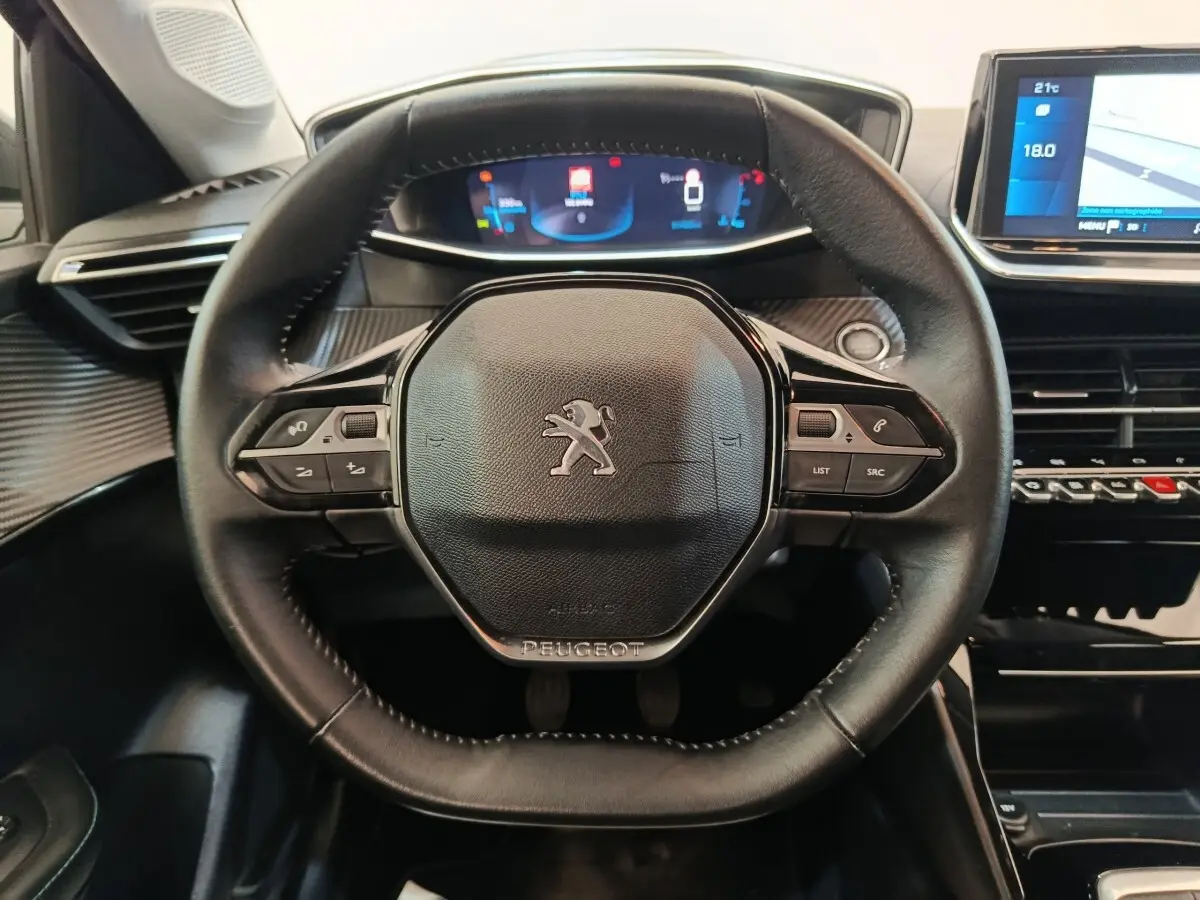 Vue rapprochée du volant cuir noir multifonctions d'une Peugeot 208 2020 avec tableau de bord numérique et écran tactile.