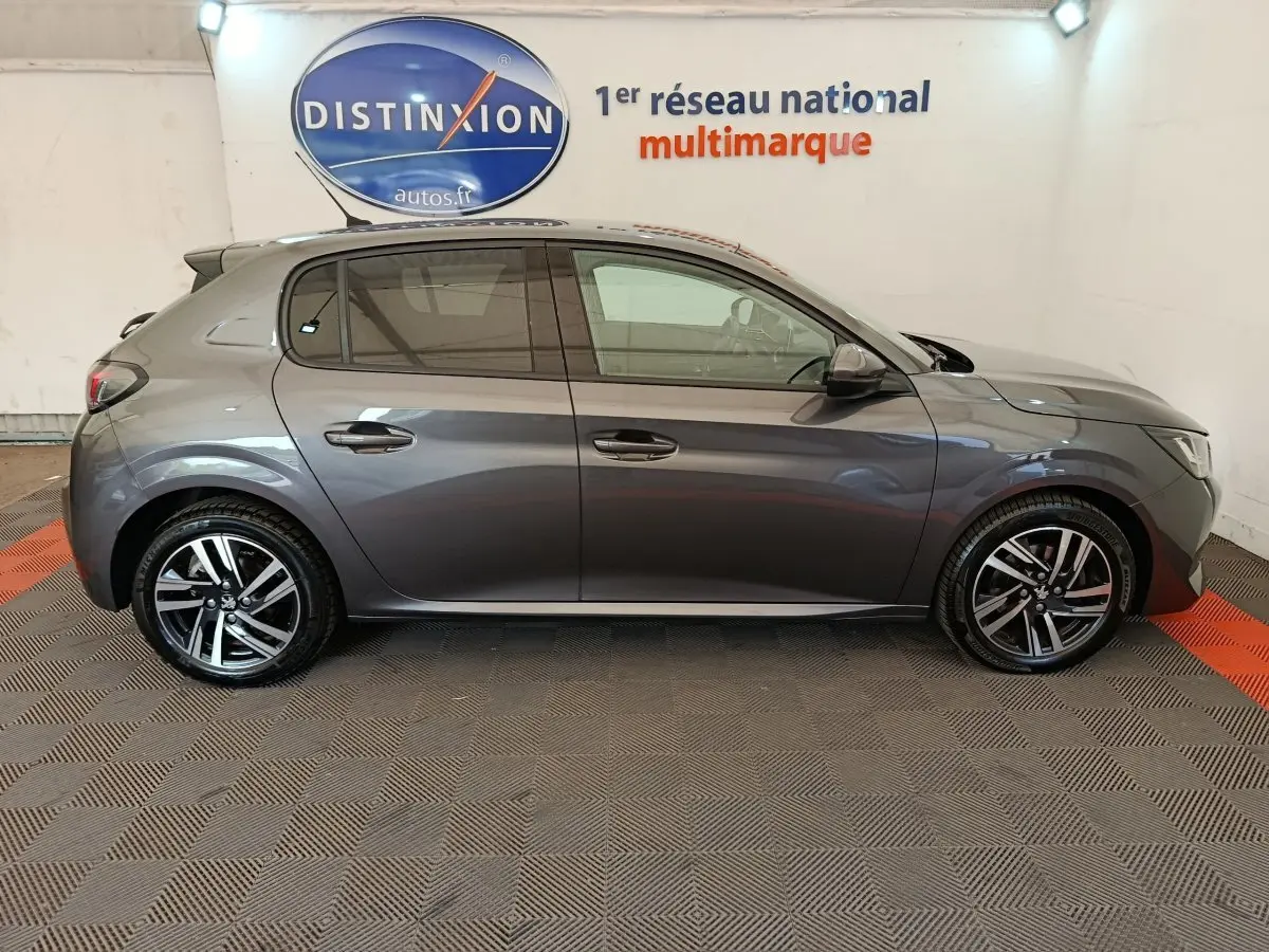 Vue latérale droite d'une Peugeot 208 gris foncé 2020 avec jantes alliage et vitres teintées en intérieur showroom.