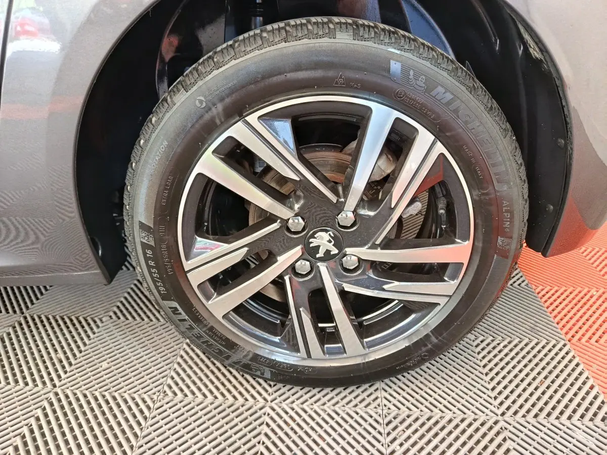 Gros plan sur la roue avant droite d'une Peugeot 208 gris métallisé avec jante alliage noire et argentée.