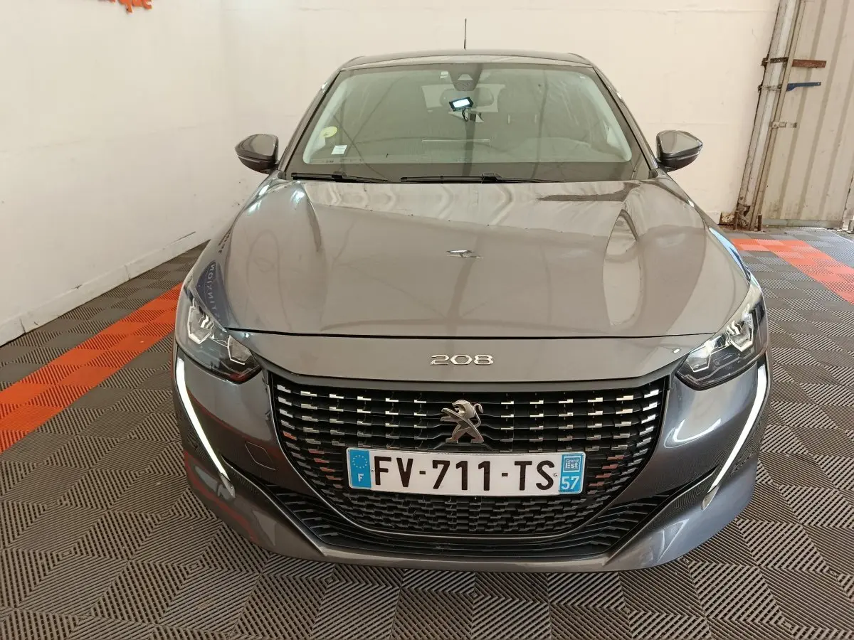 Peugeot 208 gris vue de face, avec calandre noire et feux LED en forme de griffes distinctifs.