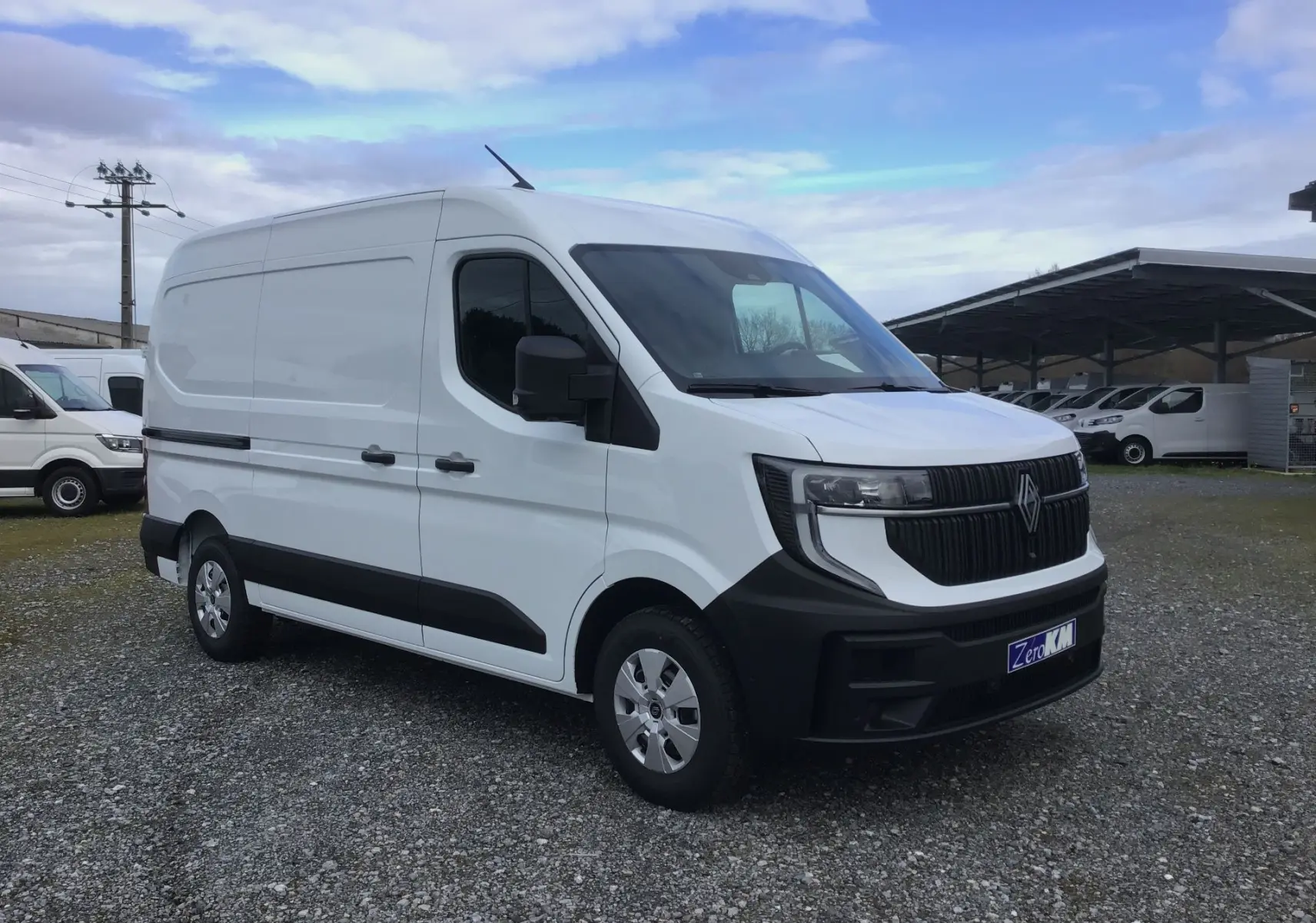 Renault Master blanc en 3/4 avant droit, avec calandre noire et jantes acier, stationné sur un sol gravillonné.