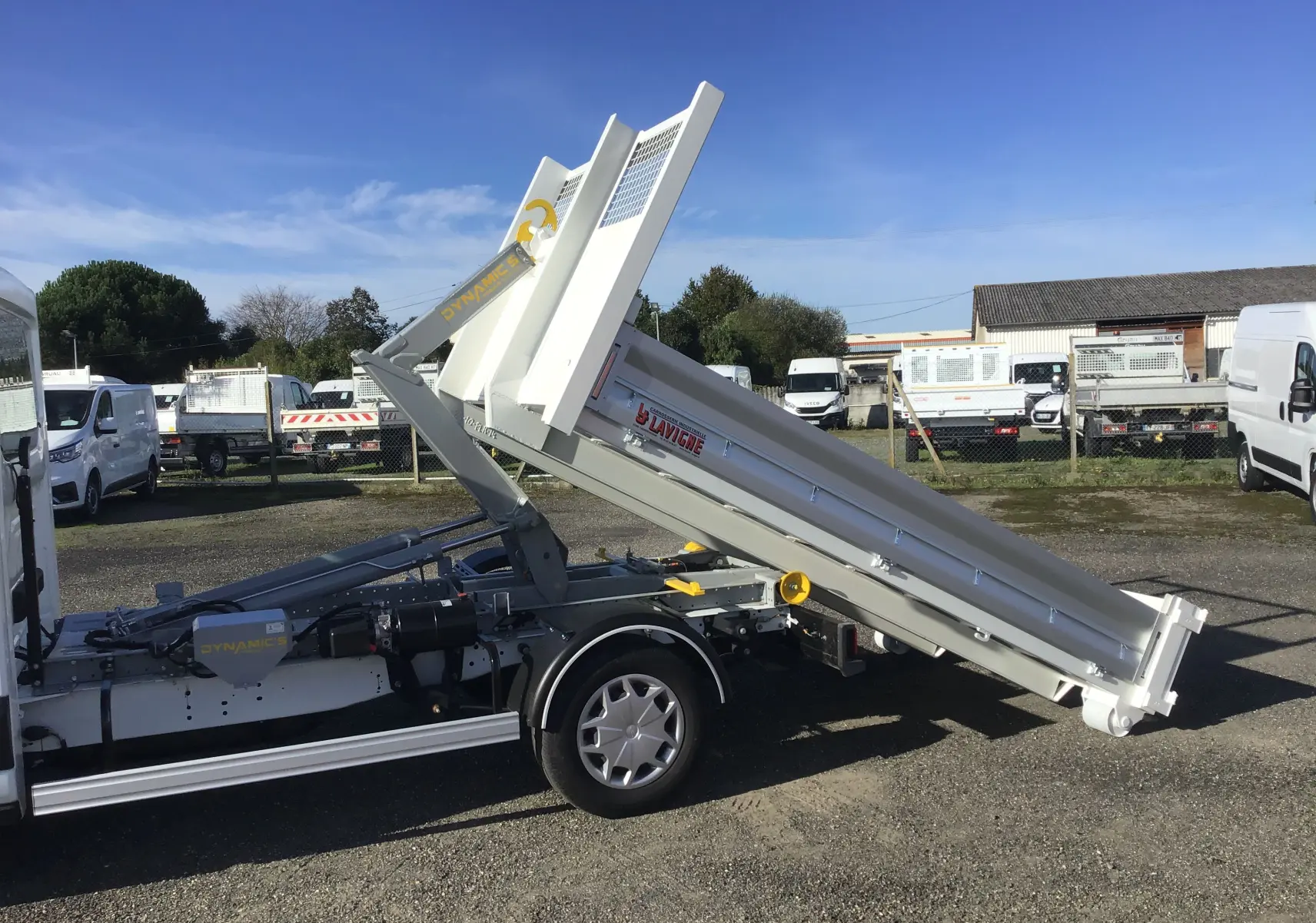 Vue latérale droite d'un Ford Transit blanc avec benne relevée et bras polybenne dynamique en extérieur.